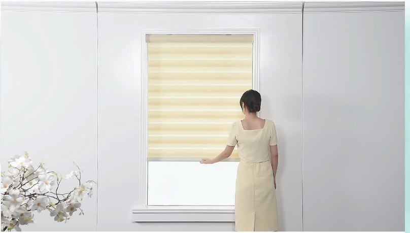 A person operating a cordless zebra blind by hand